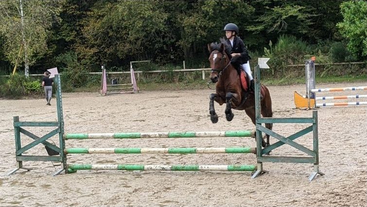 Cavalière franchissant un obstacle dans la carrière du club, par beau temps.