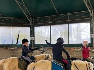 Trois enfants à poney pendant une séance de pony games, dans le manège couvert.