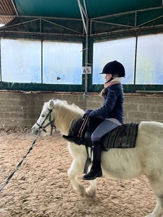 Enfant en équilibre debout sur son poney pendant un exercice de voltige.